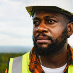 Close up portrait of black optimistic engineer man smiling and looking to the field while working outdoor.